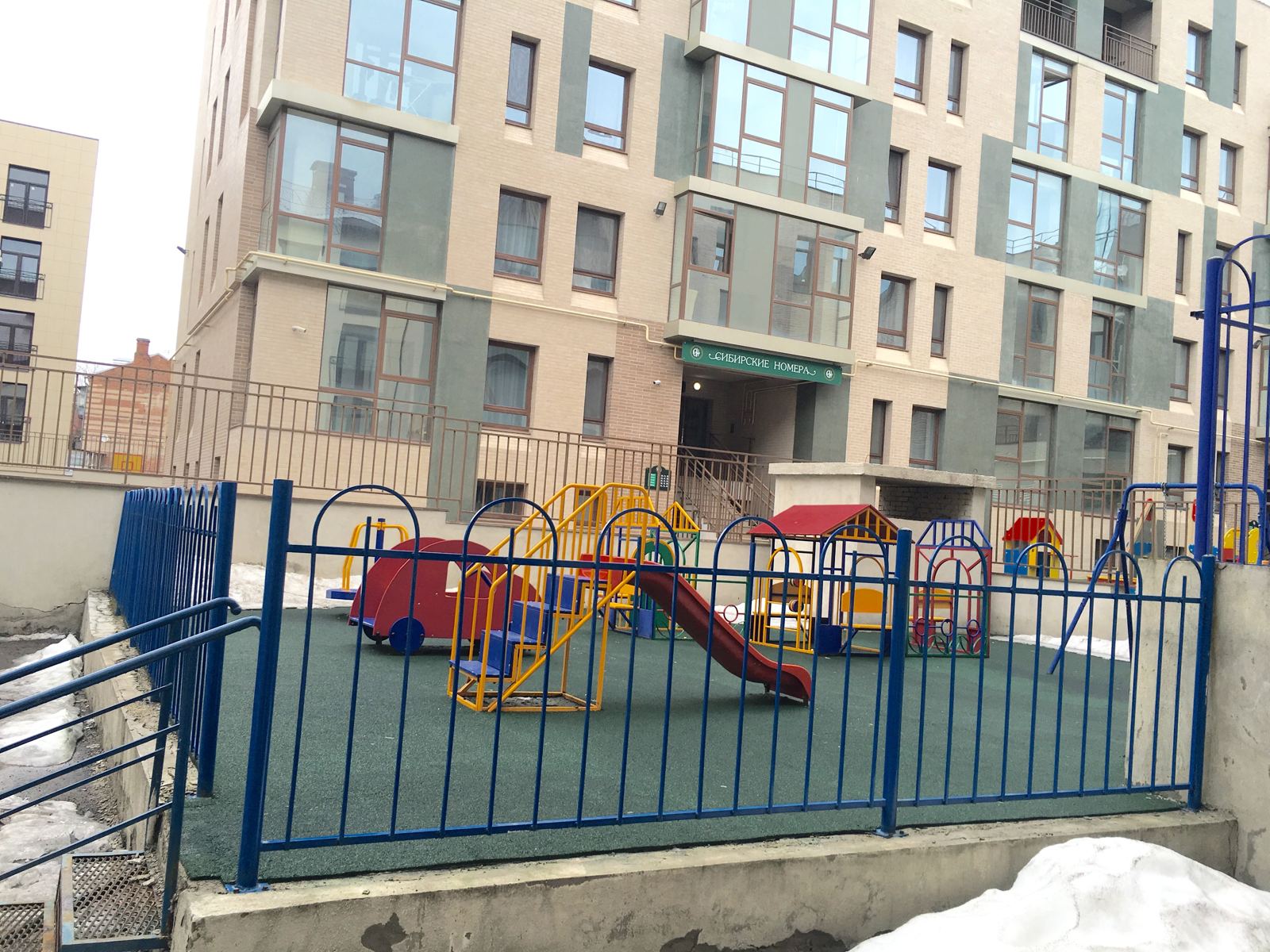 Огороженная детская площадка с мягким покрытием во дворе